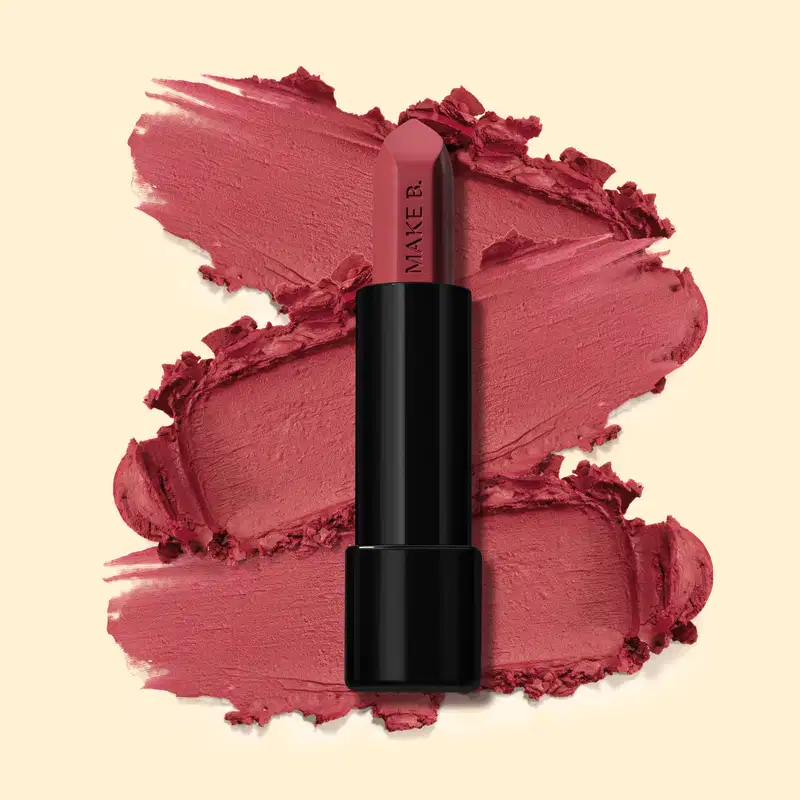 Batom mate na cor Rosa Rose Fabulous da marga Make B., em tubo preto posicionado sobre uma amostra do produto na cor rosa intenso, sobre fundo bege claro.