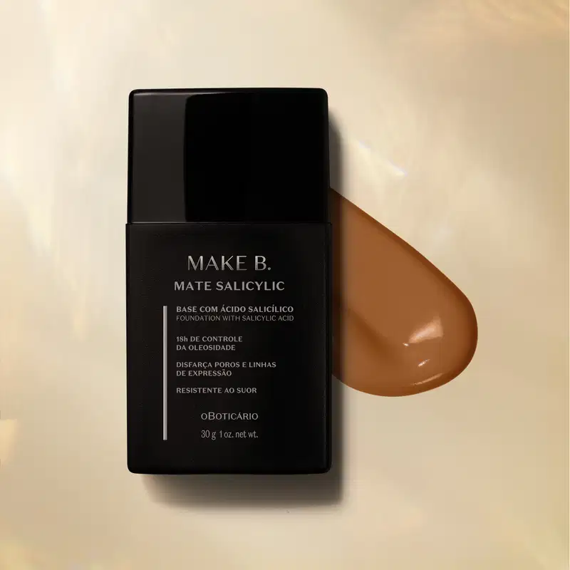 Frasco preto com letras cinzas de base líquida na cor 280 da marca Make B. Mate Salicylic sobre superfície bege com gota de produto marrom ao lado, mostrando textura e tonalidade.