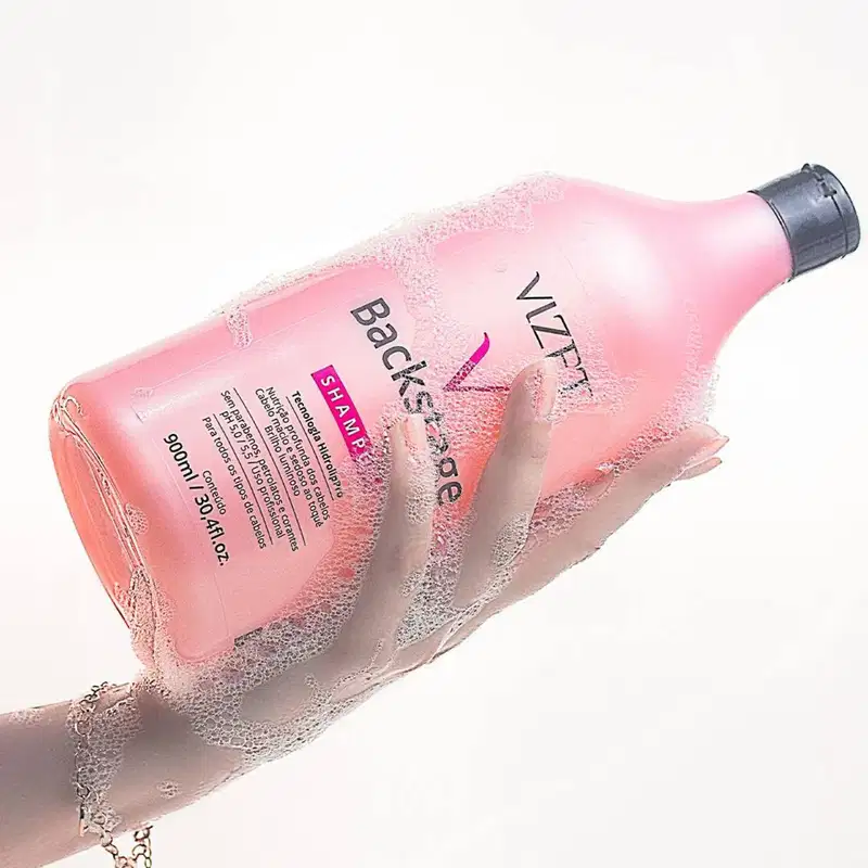 A imagem mostra uma mão ensaboada segurando o frasco com o shampoo.
