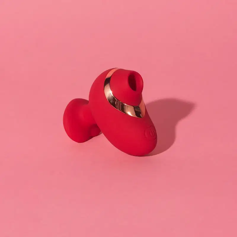 Vibrador vermelho com acabamento metálico, em formato ergonômico e compacto, da marca Désir Atelier.