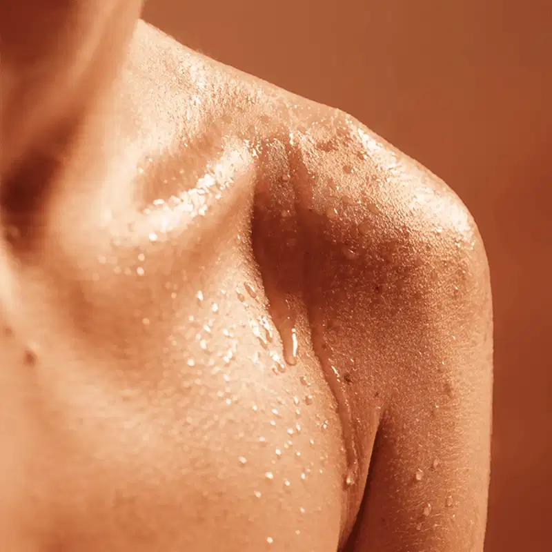 Imagem de pele com textura brilhante e úmida, com pequenas gotas de água visíveis. Sugere um produto de hidratação ou cuidado corporal da marca Skelt.