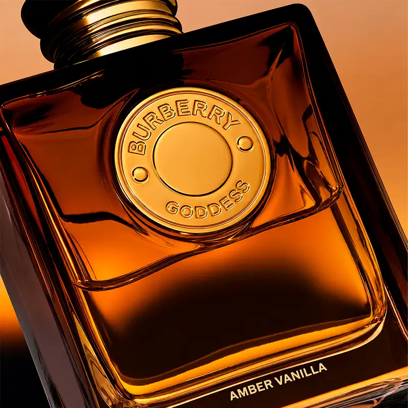 Perfume Burberry Goddess Amber Vanilla em frasco quadrado âmbar com tampa dourada. Rótulo circular dourado com inscrição "Burberry Goddess" e texto "Amber Vanilla" na base. Design luxuoso e elegante.